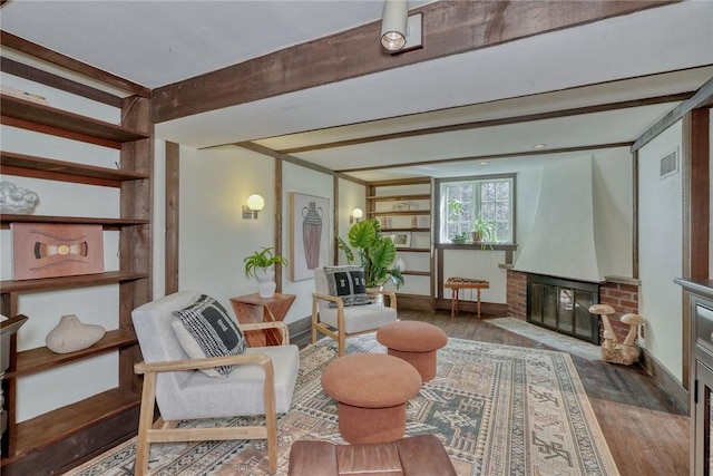 living area with beamed ceiling, a brick fireplace, baseboards, and wood finished floors