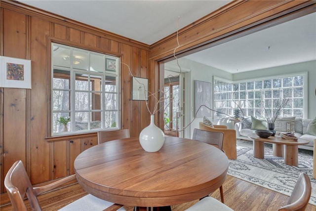 dining room with wood finished floors, a healthy amount of sunlight, and wood walls