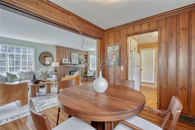 dining space with a brick fireplace, wooden walls, and light wood-style floors