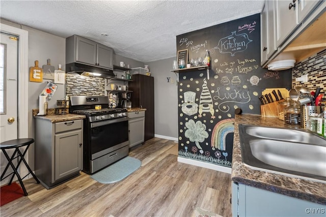 kitchen with light wood-type flooring, under cabinet range hood, a sink, backsplash, and stainless steel range with gas cooktop