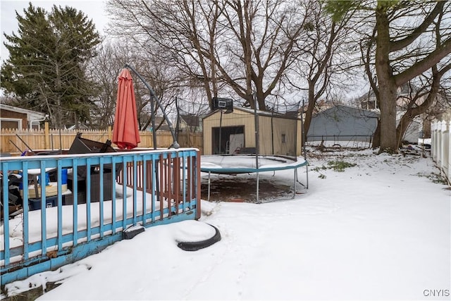 snow covered deck featuring a fenced backyard, an outbuilding, and a trampoline