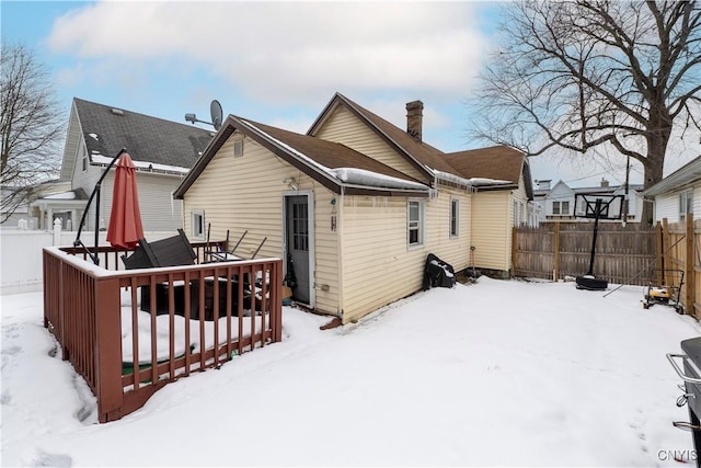 snow covered rear of property featuring a wooden deck, a fenced backyard, and a chimney