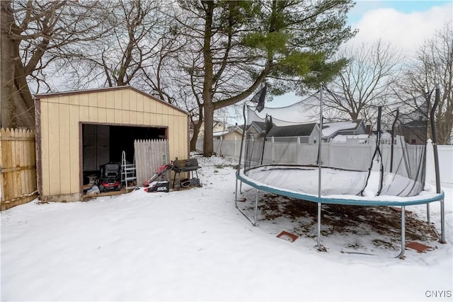 yard layered in snow with a detached garage, a trampoline, an outbuilding, and fence