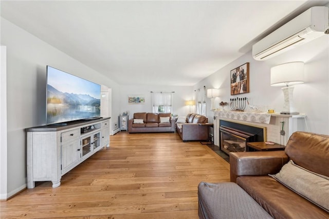 living area with a wall mounted air conditioner, baseboards, a fireplace with flush hearth, and light wood-style floors