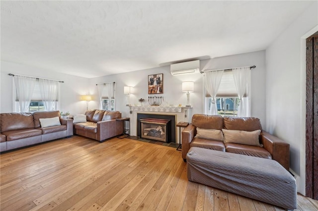 living area featuring a wealth of natural light, a fireplace with flush hearth, light wood-style flooring, and a wall unit AC