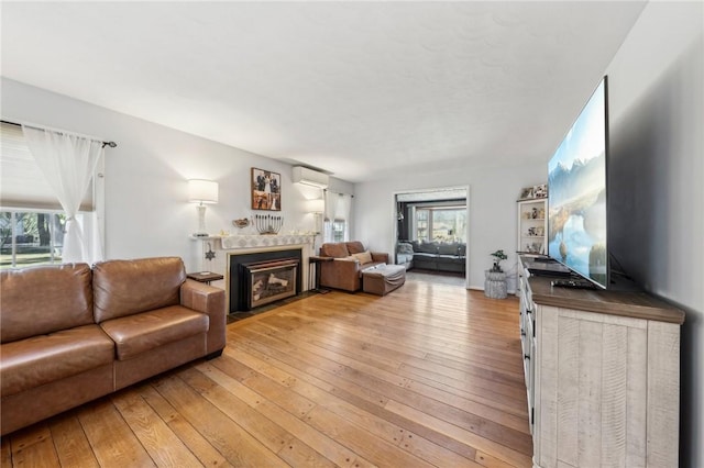 living area featuring plenty of natural light, light wood-style flooring, a wall mounted air conditioner, and a fireplace with flush hearth