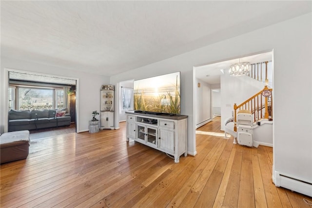 living area with a notable chandelier, light wood-style floors, a baseboard radiator, baseboard heating, and stairs