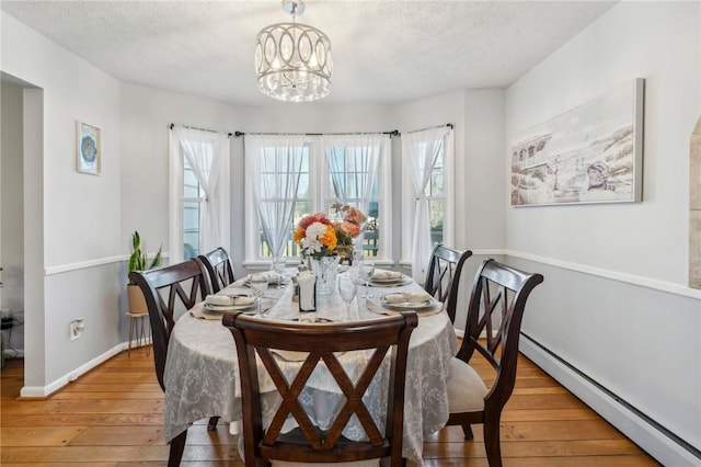 dining room featuring a notable chandelier, a textured ceiling, light wood-style floors, baseboards, and baseboard heating