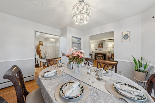 dining area featuring a chandelier, light wood finished floors, a fireplace, and a textured ceiling