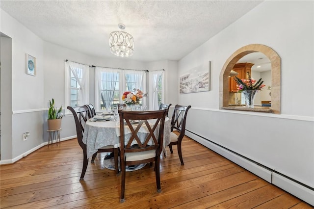 dining space with a textured ceiling, a notable chandelier, baseboard heating, and hardwood / wood-style flooring