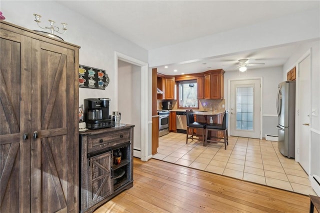 kitchen with a ceiling fan, a baseboard heating unit, stainless steel appliances, light tile patterned flooring, and decorative backsplash