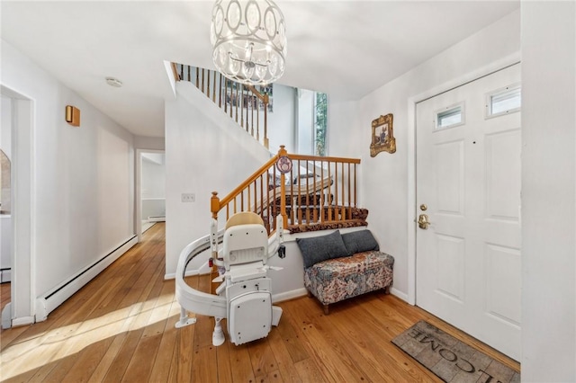 entrance foyer with a notable chandelier, baseboard heating, stairway, and hardwood / wood-style floors