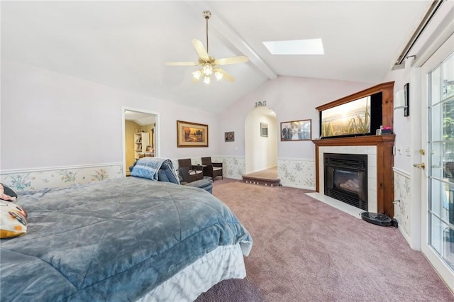 carpeted bedroom featuring vaulted ceiling with skylight, a ceiling fan, and a fireplace