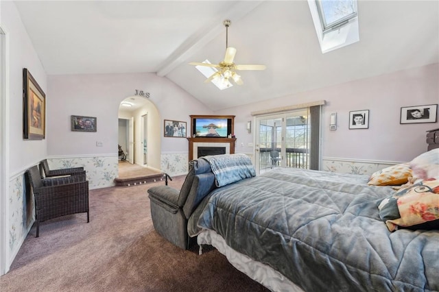 bedroom featuring a wainscoted wall, lofted ceiling with skylight, a ceiling fan, carpet floors, and access to exterior