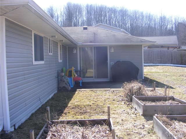 rear view of property featuring a vegetable garden and fence