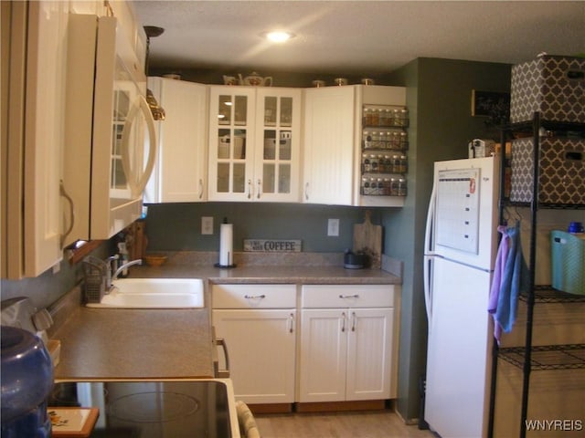 kitchen with light wood-style flooring, a sink, freestanding refrigerator, white cabinetry, and glass insert cabinets