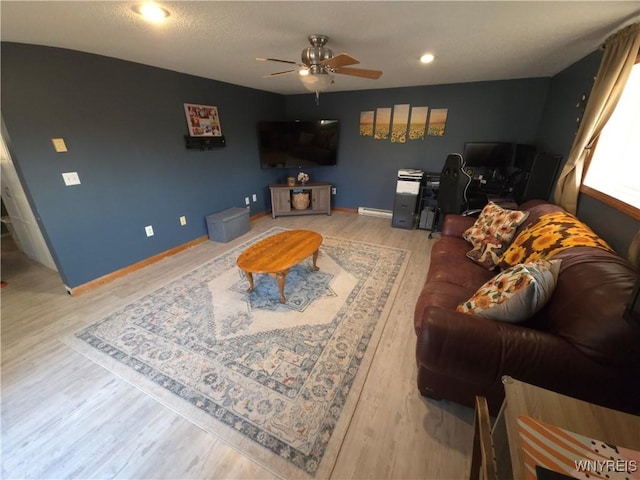 living area with baseboards, a baseboard heating unit, light wood-type flooring, and a ceiling fan