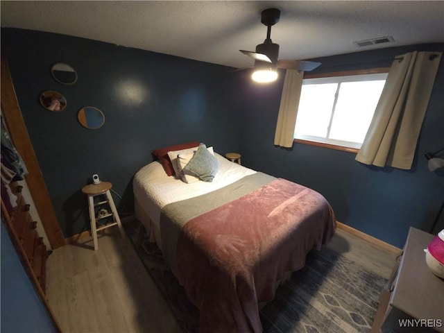 bedroom with ceiling fan, visible vents, baseboards, and wood finished floors