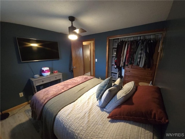 bedroom with a ceiling fan, wood finished floors, baseboards, and a closet