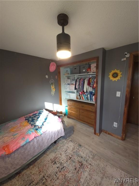 bedroom featuring a closet, baseboards, a textured ceiling, and light wood-style floors