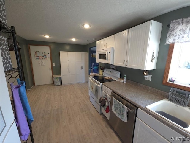 kitchen with light wood-style flooring, a sink, a textured ceiling, white cabinetry, and white appliances