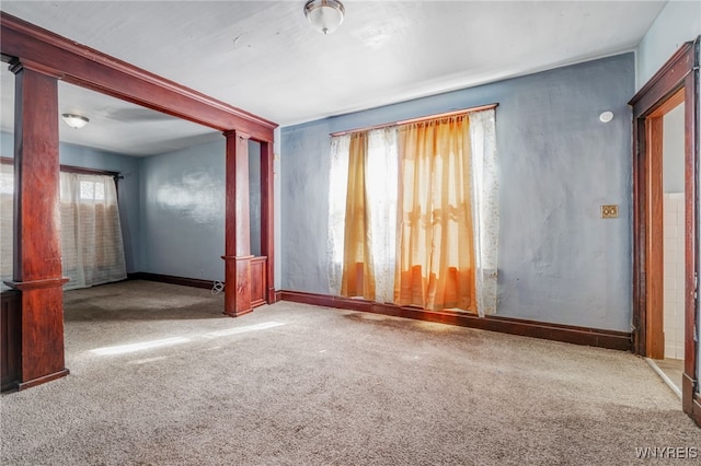 carpeted spare room featuring baseboards and decorative columns