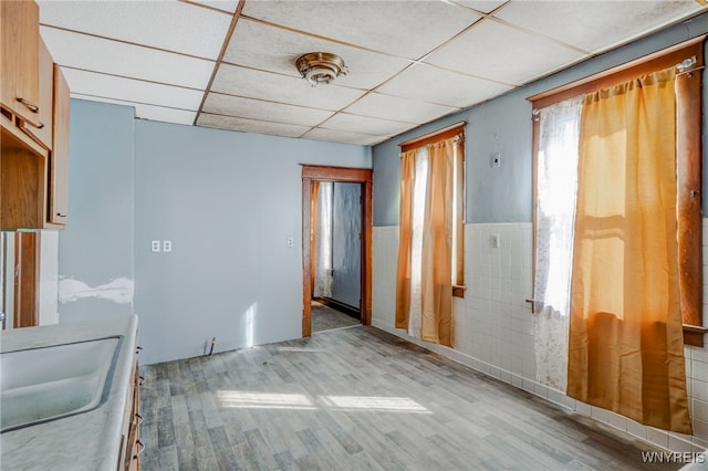 kitchen featuring a wainscoted wall, wood finished floors, tile walls, a paneled ceiling, and a sink