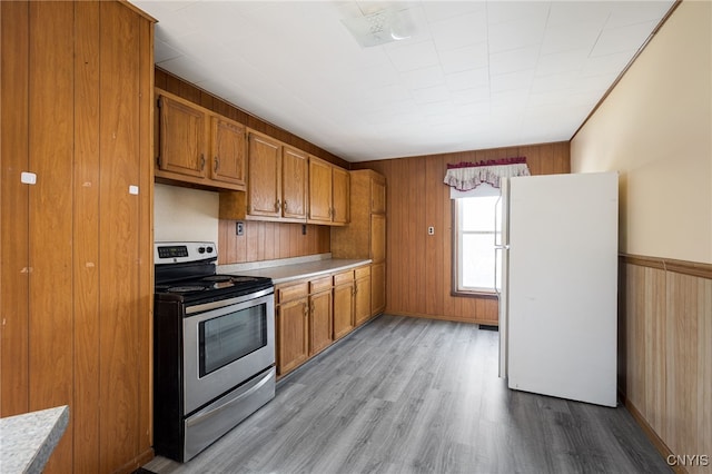 kitchen featuring electric range, wood finished floors, brown cabinets, and freestanding refrigerator