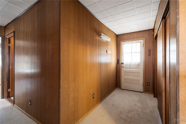 hall featuring baseboards, carpet floors, and wood walls