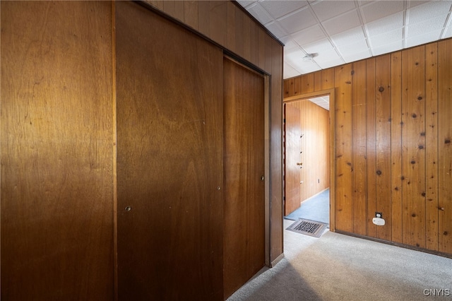 corridor featuring visible vents, wooden walls, and carpet flooring