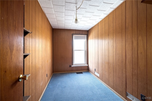 spare room with visible vents, baseboards, wood walls, and carpet flooring