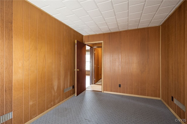 unfurnished room with carpet, visible vents, wood walls, and baseboards