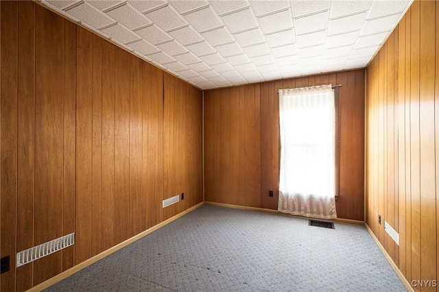 carpeted empty room with baseboards, visible vents, and wood walls