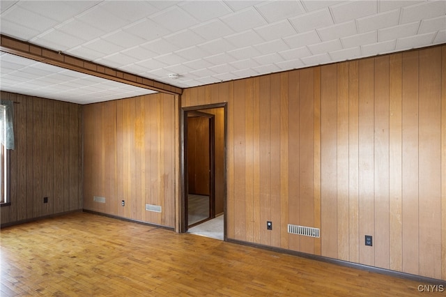 spare room featuring visible vents, wood walls, baseboards, and wood finished floors