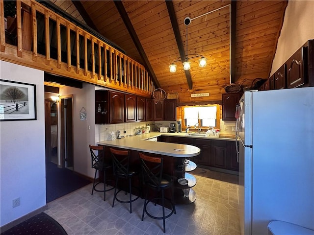 kitchen featuring a peninsula, beam ceiling, freestanding refrigerator, decorative backsplash, and dark brown cabinets