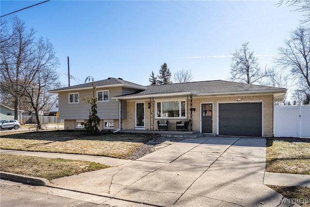 split level home featuring brick siding, an attached garage, driveway, and fence