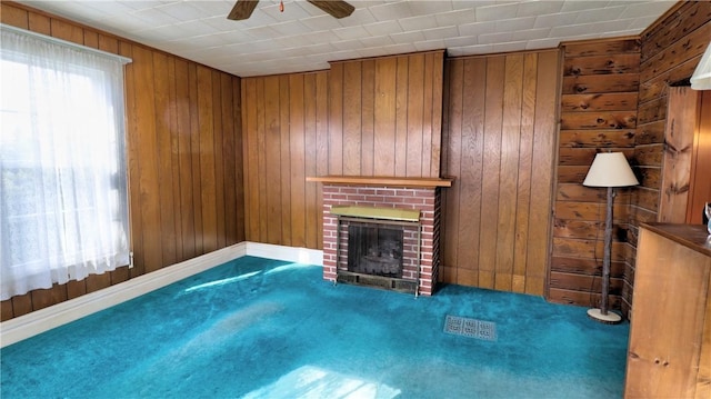 unfurnished living room with a brick fireplace, carpet, wood walls, and ceiling fan