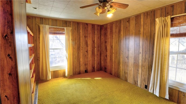 carpeted spare room with wooden walls and a ceiling fan