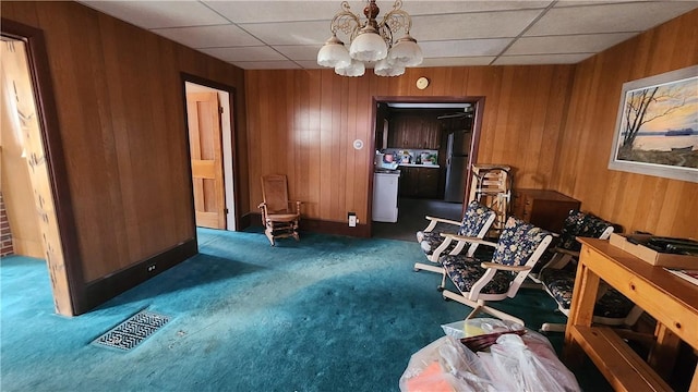 interior space featuring a chandelier, carpet, wood walls, and a paneled ceiling