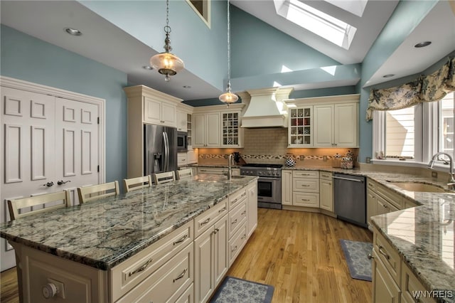 kitchen featuring premium range hood, stainless steel appliances, cream cabinets, and a sink