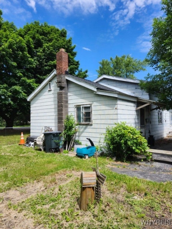 view of home's exterior with fence, a lawn, and a chimney