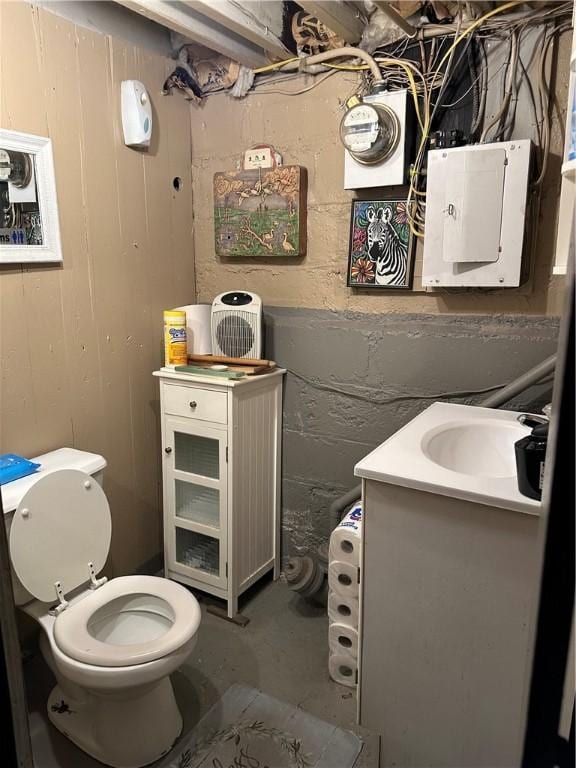 half bathroom featuring electric panel, vanity, toilet, and concrete block wall