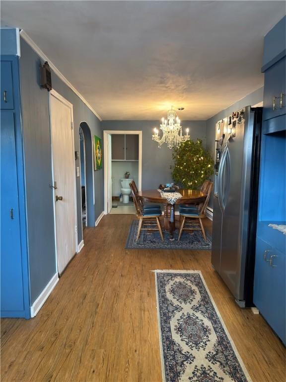 dining space with arched walkways, a chandelier, crown molding, and wood finished floors