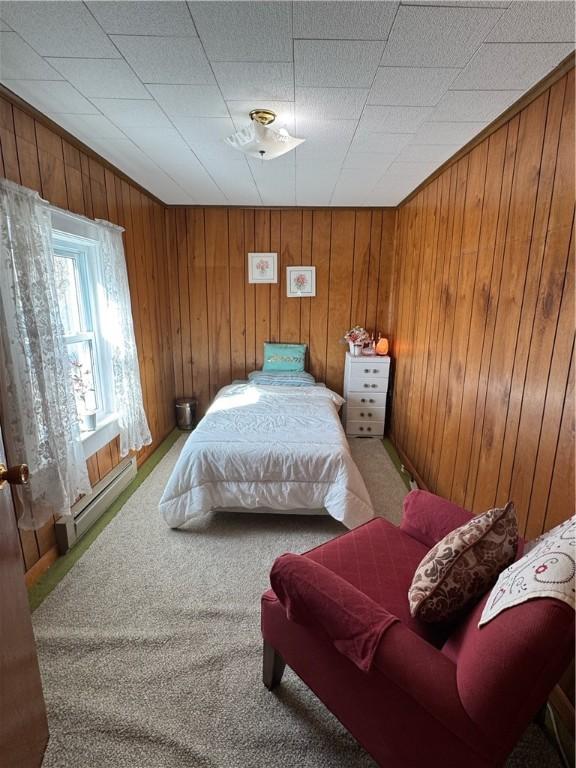 bedroom with light colored carpet, baseboard heating, and wooden walls