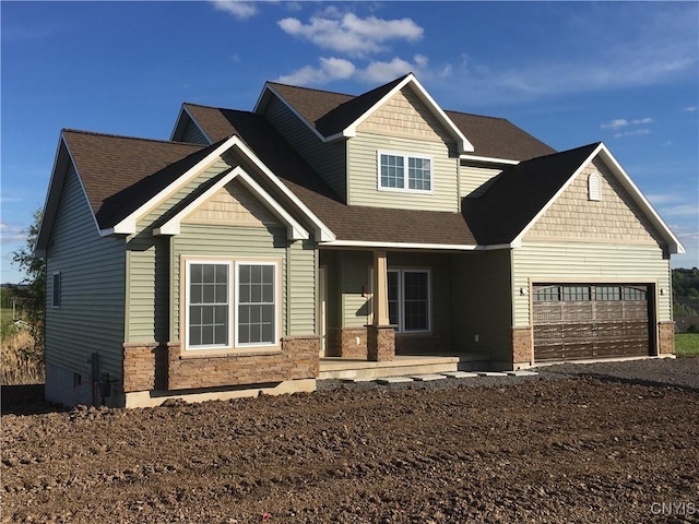 craftsman house with driveway, an attached garage, covered porch, a shingled roof, and stone siding