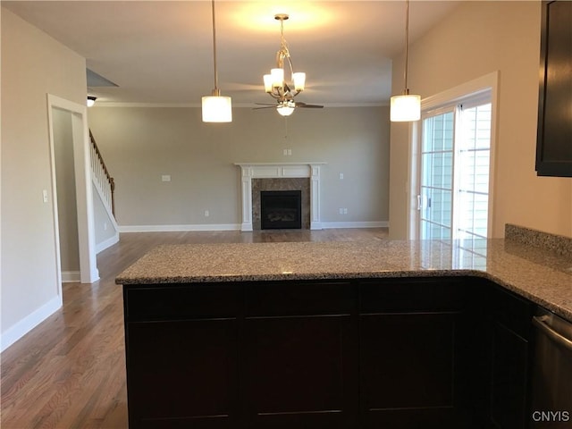 kitchen with a fireplace with flush hearth, wood finished floors, a peninsula, light stone countertops, and ceiling fan