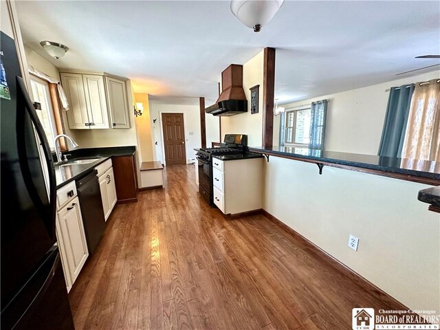 kitchen featuring premium range hood, black appliances, a sink, dark countertops, and dark wood-style floors