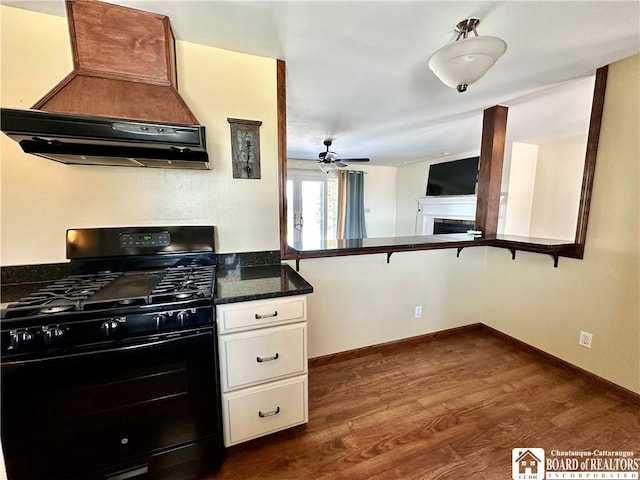 kitchen with black gas range oven, dark wood-type flooring, premium range hood, a fireplace, and white cabinetry