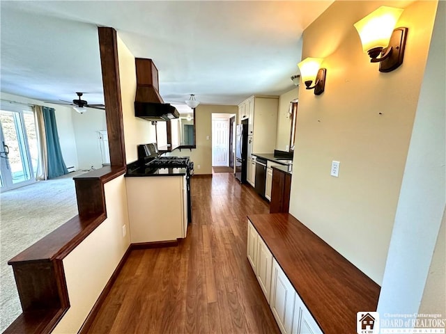 kitchen featuring dishwashing machine, ventilation hood, stainless steel range with gas stovetop, freestanding refrigerator, and dark countertops