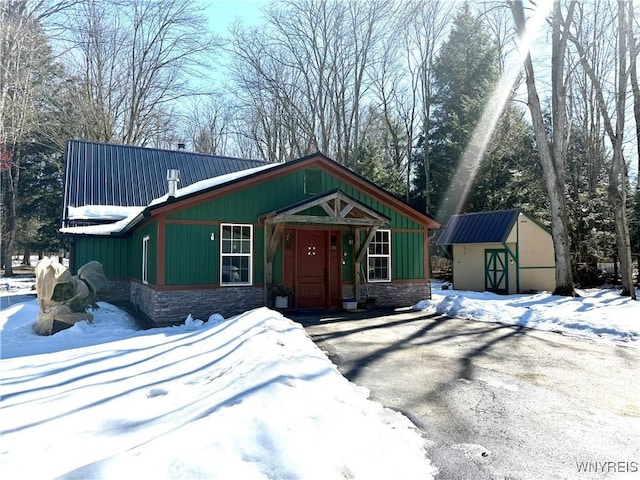 view of front of property featuring board and batten siding, metal roof, a storage shed, an outbuilding, and stone siding